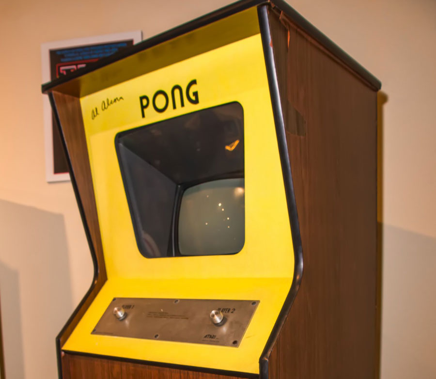 A photo of a vintage pong arcade machine. The sides are faux wood and the front is yellow. There is a cathode ray tube monitor visible