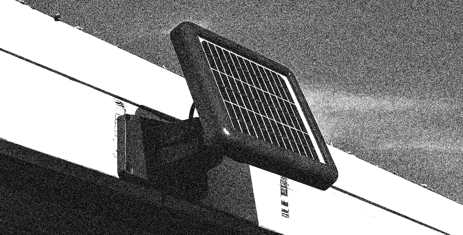 A grainy black-and-white image of a solar panel on the eaves of a house.